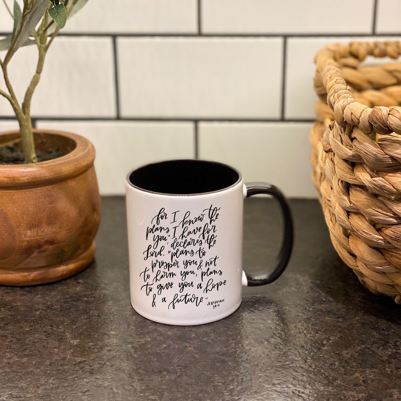 May include: White ceramic mug with a black rim and handle. The mug has black lettering that reads "for I know the plans I have for you, declares the Lord, "plans to prosper you not to harm you, plans to give you a hope & a future." Jeremiah 29:11