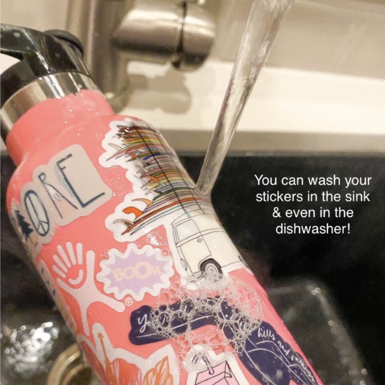 May include: A pink stainless steel water bottle with various colorful stickers, including a surfboard, a van, and the word "BOOM". Water is being poured over the bottle, demonstrating that the stickers are waterproof. The text "You can wash your stickers in the sink & even in the dishwasher!" is visible in the image.