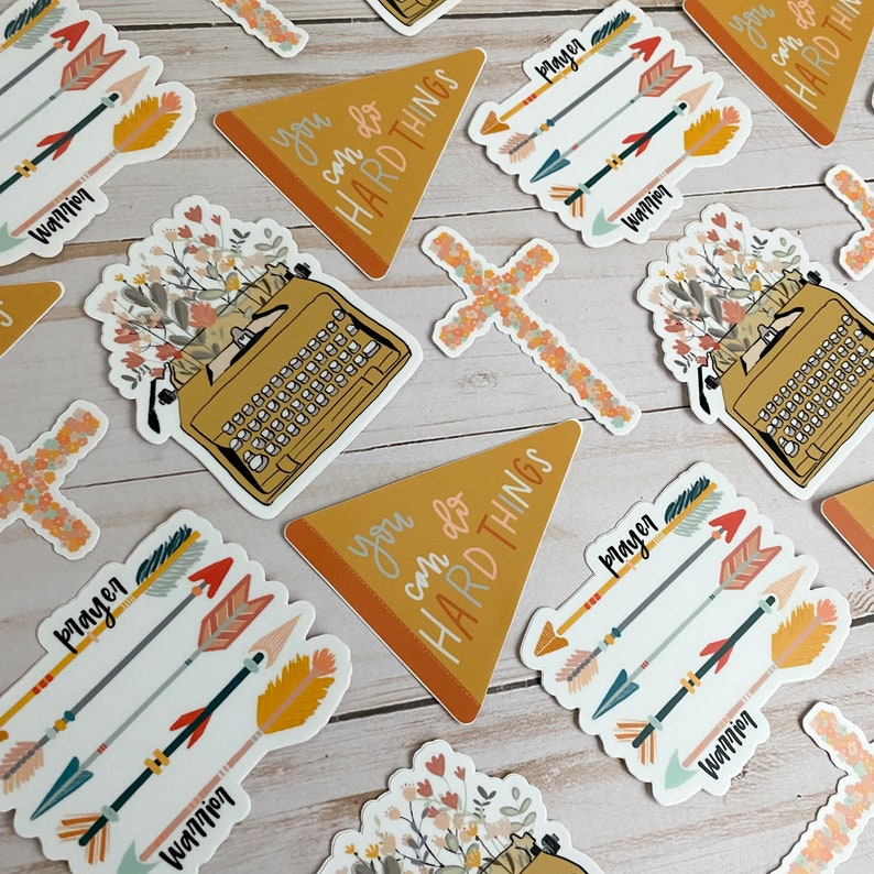 May include: A set of colourful stickers with inspirational messages. The stickers feature a typewriter, arrows, a cross, and the phrase "you can do hard things".