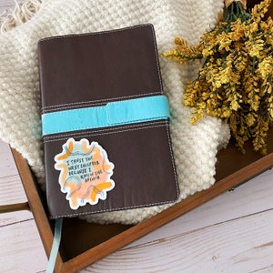 May include: A brown leather journal with a turquoise strap and a sticker that says "I trust the next chapter because I know the author".