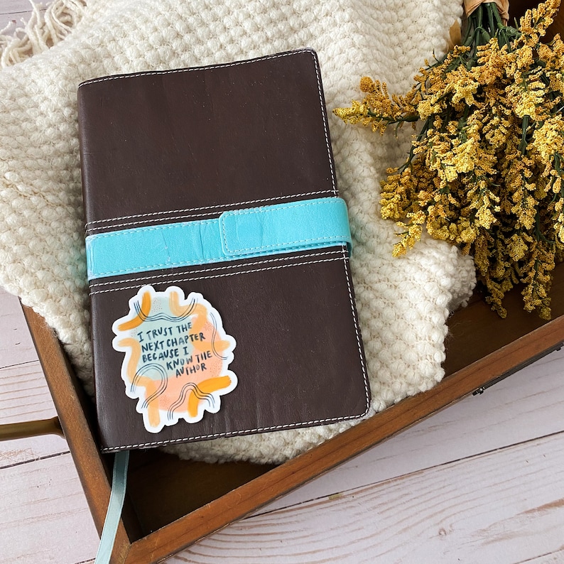 May include: A brown leather journal with a turquoise strap and a sticker that says "I trust the next chapter because I know the author".