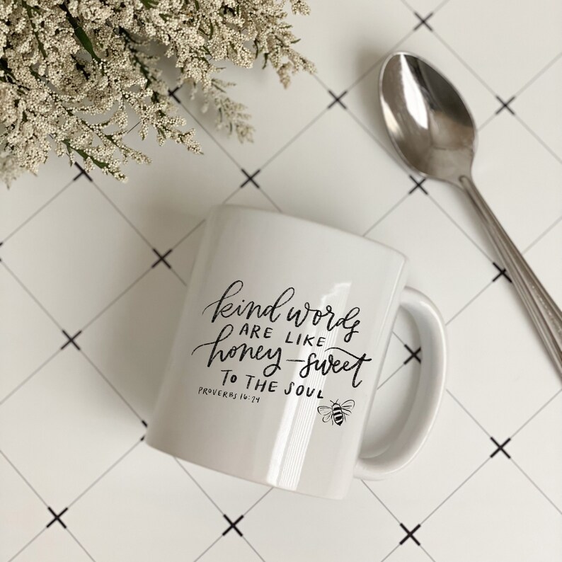 May include: White ceramic mug with black text that reads "Kind words are like honey-sweet to the soul" and a small bee graphic. The text also includes the scripture reference "Proverbs 16:24".