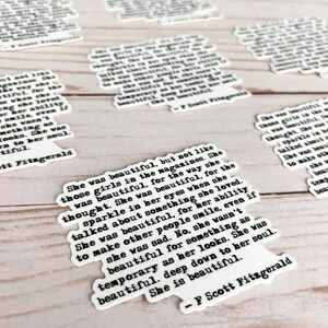 May include: A white sticker with black text featuring a quote by F. Scott Fitzgerald. The quote reads: "She was beautiful, but not like those girls in the magazines. She was beautiful, for the way she thought. She was beautiful, for the sparkle in her eyes when she talked about something she loved. She was beautiful, for her ability to make other people smile, even if she was sad. No, she wasn't beautiful for something as temporary as her looks. She was beautiful. Deep down to her soul. She is beautiful."