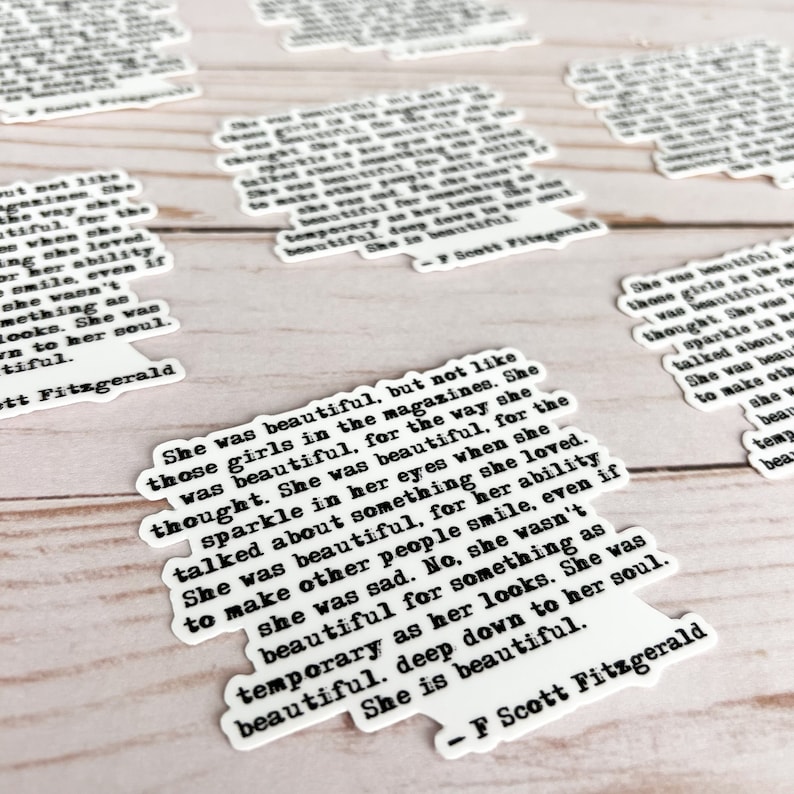 May include: A white sticker with black text featuring a quote by F. Scott Fitzgerald. The quote reads: "She was beautiful, but not like those girls in the magazines. She was beautiful, for the way she thought. She was beautiful, for the sparkle in her eyes when she talked about something she loved. She was beautiful, for her ability to make other people smile, even if she was sad. No, she wasn't beautiful for something as temporary as her looks. She was beautiful. Deep down to her soul. She is beautiful."