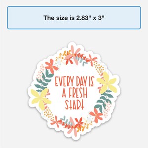Peut inclure: Un autocollant blanc avec une bordure de couronne florale dans des tons de rose, jaune et vert. Le texte "EVERY DAY IS A FRESH START" est au centre en rouge.