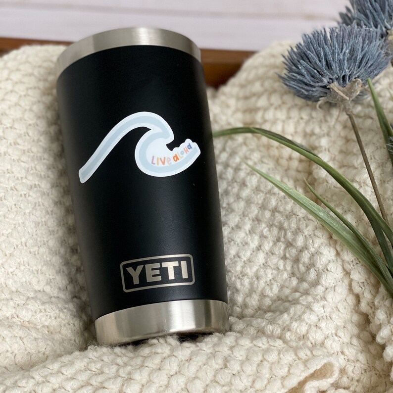 May include: A black Yeti tumbler with a white wave sticker and the text "Live a little" in rainbow colors.