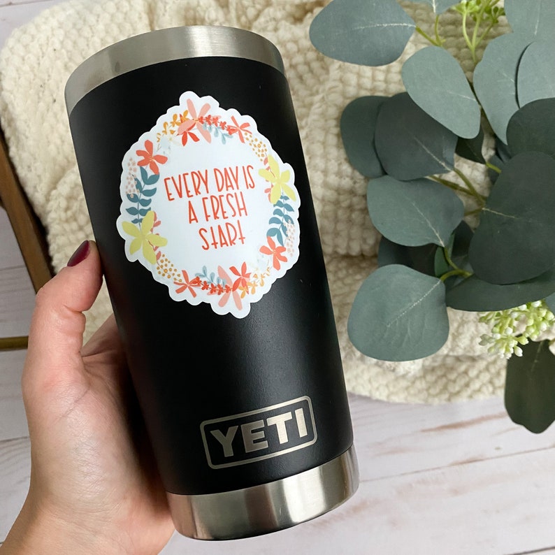 Peut inclure: Un gobelet Yeti noir avec un autocollant blanc qui dit "Every day is a fresh start" entour&eacute; de fleurs color&eacute;es.
