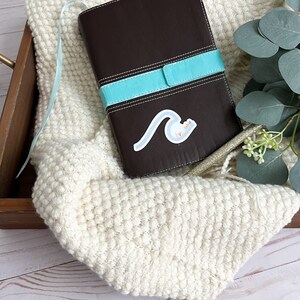 May include: A brown leather-bound journal with a turquoise blue ribbon closure. A sticker with a blue wave and the text "Live Aloha" is on the front cover.