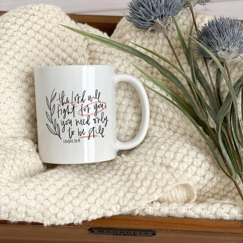Op de afbeelding: Witte keramische mok met zwarte kalligrafie die "De Heer zal voor je vechten, je hoeft alleen maar stil te zijn" en "Exodus 14:14" zegt.