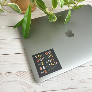 May include: A black square sticker with colourful text that reads "You go before me and behind me" with the scripture reference "Psalm 139:5" written in cursive.