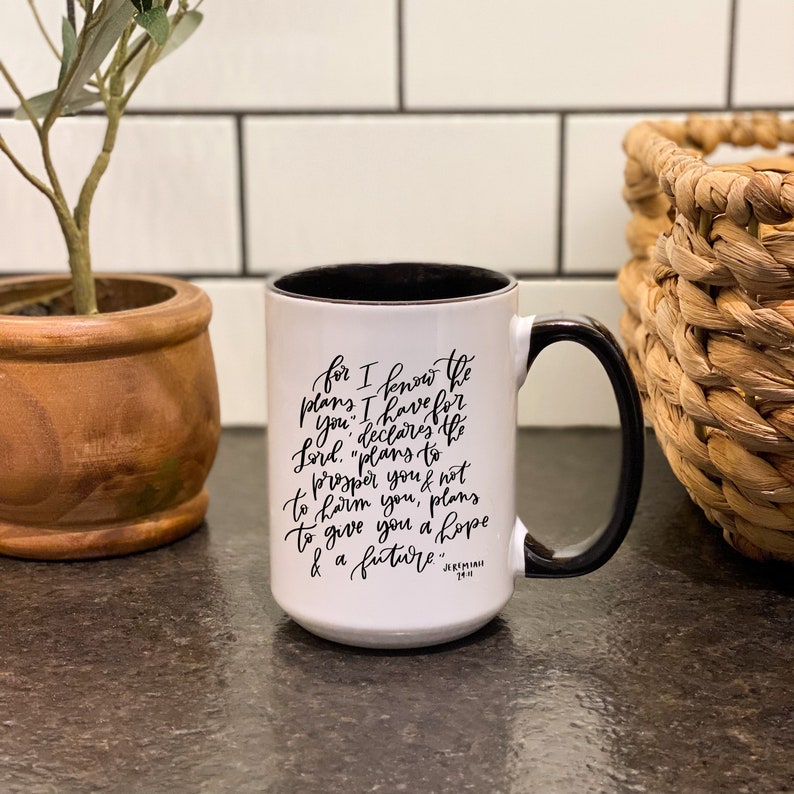 May include: White ceramic mug with a black handle and black interior. The mug has a black inscription that reads "for I know the plans I have for you, declares the Lord. "plans to prosper you & not to harm you, plans to give you a hope & a future." Jeremiah 29:11