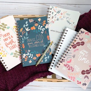 May include: Four different spiral bound notebooks with floral designs and inspirational quotes. The quotes are "Every day is a fresh start", "Praise God from whom all blessings flow", "Where God guides", and "One day at a time".
