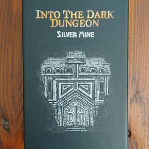 May include: A black box with gold and white text reading "Into The Dark Dungeon" and "Silver Mine". The box has a grayscale illustration of a building with an arched doorway and detailed stonework.