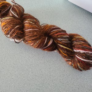 May include: A skein of brown yarn with multi-colored stripes of white, orange, red, and green. The yarn is soft and fluffy, and it would be perfect for knitting or crocheting.