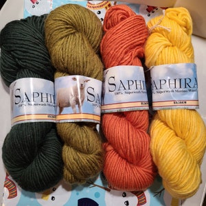 May include: Four skeins of yarn in green, olive green, orange, and yellow. The yarn is labeled "Saphira 100% Superwash Merino Wool".