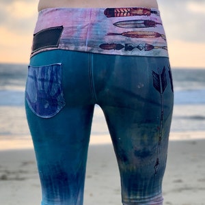May include: Blue tie-dye bell bottom pants with a black waistband and a Native American inspired design featuring arrows and a headdress.