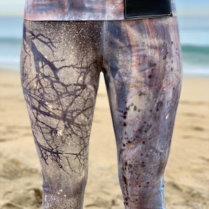 May include: Purple and gray leggings with a white and black splatter paint design. The leggings have a wide waistband with a black leather patch.