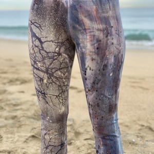 May include: High-waisted leggings with a blue, purple, and white tie-dye pattern. The leggings have a gold logo on the waistband that says "Artisan Handmade".