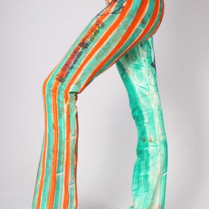 Op de afbeelding: Een gestreepte broek met een wijde pijp. De broek is oranje en turquoise met een witte tailleband.