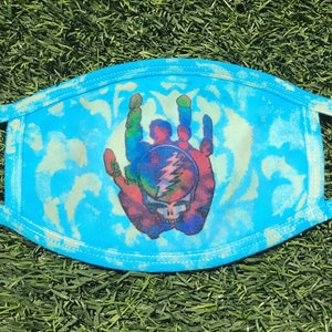 May include: A blue face mask with a tie-dye pattern and a Grateful Dead Steal Your Face logo printed on it.