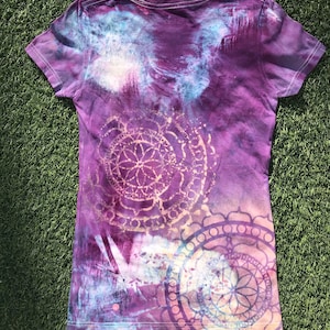 May include: Purple tie-dye t-shirt with a white and gold mandala design. The shirt has a relaxed fit and a crew neck.