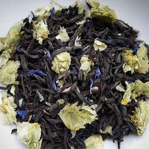 May include: A close-up of a blend of black tea leaves, dried cornflower petals, and dried green leaves. The tea leaves are dark brown and black, the cornflower petals are a vibrant blue, and the green leaves are a light green.
