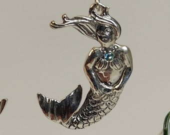 Puede incluir: Pendientes de plata de sirena con detalles de piedras preciosas azules. Las sirenas tienen escamas detalladas y cabello fluido.