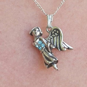 May include: A silver necklace with a pendant of an angel with blue crystal accents.