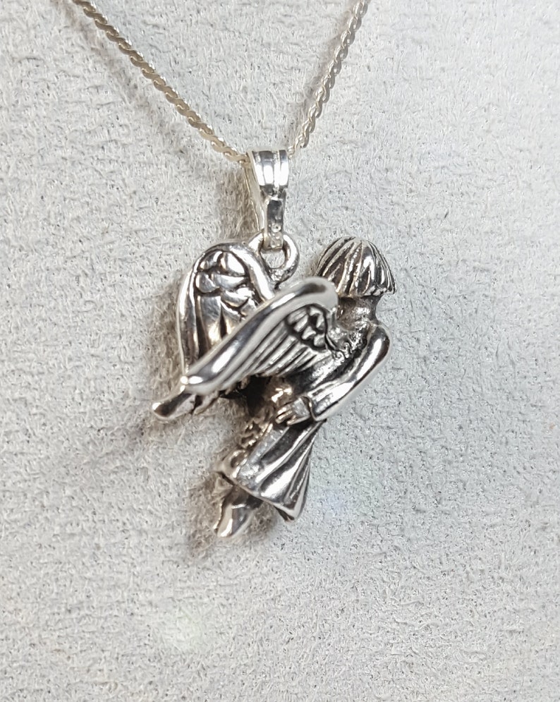 May include: Silver pendant necklace featuring a detailed angel with wings outstretched. The angel is depicted in a flying pose, with its head tilted downwards.