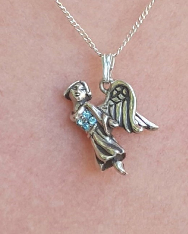 May include: A silver necklace with a pendant of an angel with blue crystal accents.