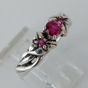 May include: A silver ring with a twisted band and three pink gemstones. The largest gemstone is in the center and the two smaller gemstones are on either side.