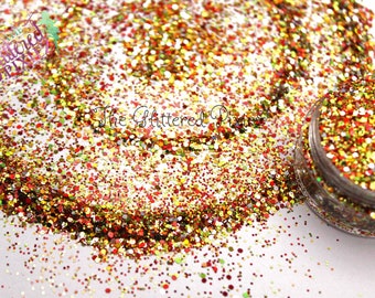 Könnte beinhalten: Nahaufnahme eines Glases mit rotem, goldenem, grünem und weißem Glitter. Der Glitter ist um das Glas herum auf einer weißen Oberfläche verstreut. Der Text "The Glittered Pixie" ist auf dem Glas sichtbar.