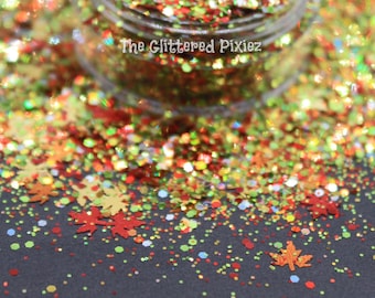 Könnte beinhalten: Nahaufnahme eines Glases mit rotem, orangefarbenem, gelbem und grünem Glitter in verschiedenen Formen, darunter kleine Kreise und Blätter. Der Glitter ist auf einer schwarzen Oberfläche verstreut.