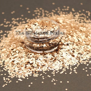 May include: A close-up of a jar filled with gold glitter. The glitter is a mix of small and large pieces, and it is scattered around the jar on a dark surface. The text "The Glittered Pixiez" is visible on the jar.