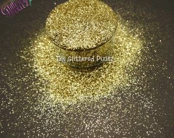 May include: A close-up of a jar of fine gold glitter. The glitter is loose and scattered around the jar, creating a shimmering effect.
