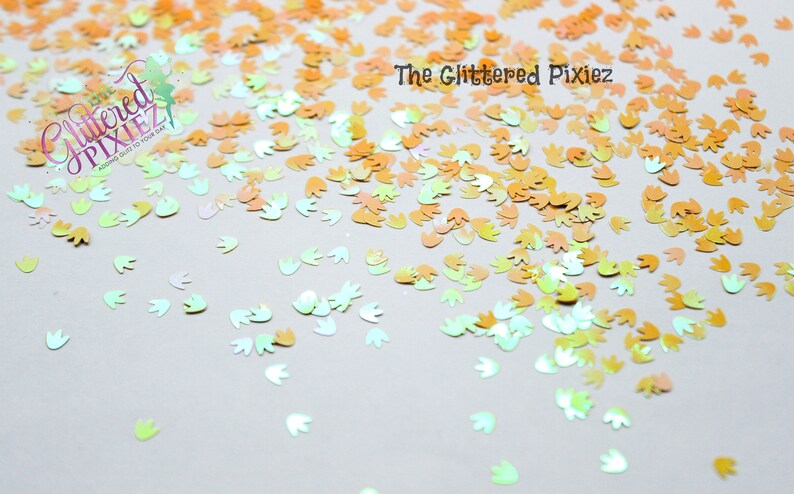 May include: A scattering of iridescent, pastel-colored, flower-shaped glitter. The glitter is a mix of light green, light blue, and light orange.