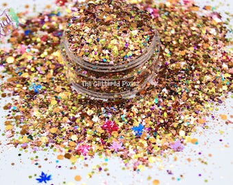 Op de afbeelding: Een close-up van een pot gevuld met verschillende glitters in goud, roze, groen, blauw en paars. De glitter is rond de pot verspreid op een wit oppervlak. De pot heeft een label met de tekst "The Glittered Pixiez".