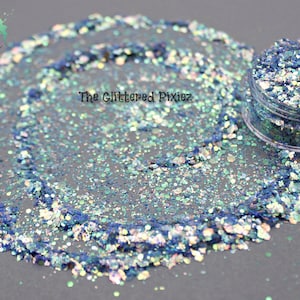 May include: A small jar of iridescent blue and green glitter with a white background. The glitter is scattered around the jar.