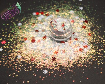May include: A jar of iridescent glitter with a mix of red, white, and gold glitter flakes. The glitter is scattered around the jar on a black surface. The jar has a label that reads "The Glittered Pixie".
