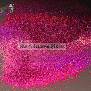 May include: A close-up of a pile of iridescent pink glitter with a purple sheen. The glitter is scattered on a black surface. The text "The Glittered Pixiez" is visible in the lower center of the image.