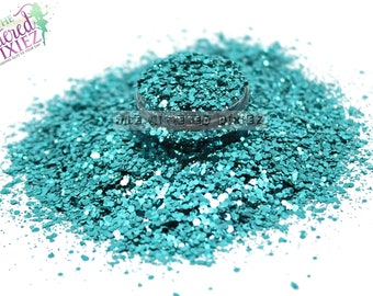 May include: A pile of teal glitter with a small sample jar in the center. The glitter is a mix of small and large flakes.