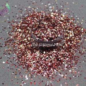 May include: A close-up of a jar of red, gold, and white glitter. The glitter is scattered around the jar on a gray surface.