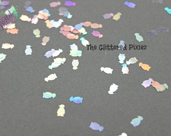 May include: A scattering of iridescent penguin-shaped glitter on a dark gray background. The glitter is a mix of light blue, pink, and purple.