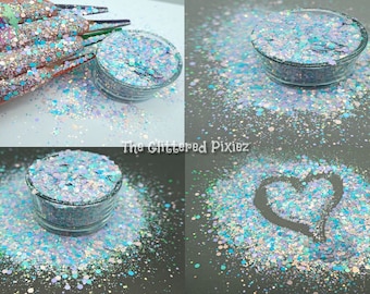 Puede incluir: Primer plano de un tarro de purpurina iridiscente con una mezcla de colores azules, blancos y rosas. La purpurina está esparcida alrededor del tarro, creando un efecto brillante y colorido.