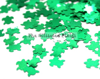 May include: Green glitter shaped like turtles. The glitter is scattered on a white background.