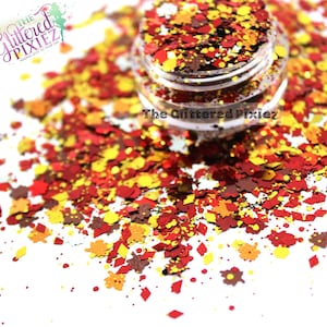 May include: A jar filled with autumn-themed glitter in shades of red, yellow, and brown. The glitter is scattered around the jar, with leaf and diamond shapes. The text "The Glittered Pixiez" is visible.