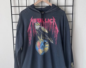 Puede incluir: Sudadera negra de manga larga con capucha con un gráfico vintage de Metallica que presenta un águila posada sobre un globo terráqueo. El gráfico es en rojo, blanco y azul con efectos de pintura que gotean. El texto "Metallica" está impreso en blanco.