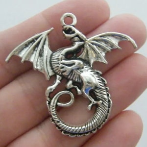 May include: Silver-toned dragon charm with wings outstretched and tail curled. The dragon is detailed with scales and has a loop at the top for attaching to a necklace or bracelet.