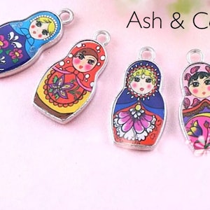 May include: Four silver charm pendants featuring Russian nesting dolls. Each doll is painted with a different colorful design and has a smiling face.