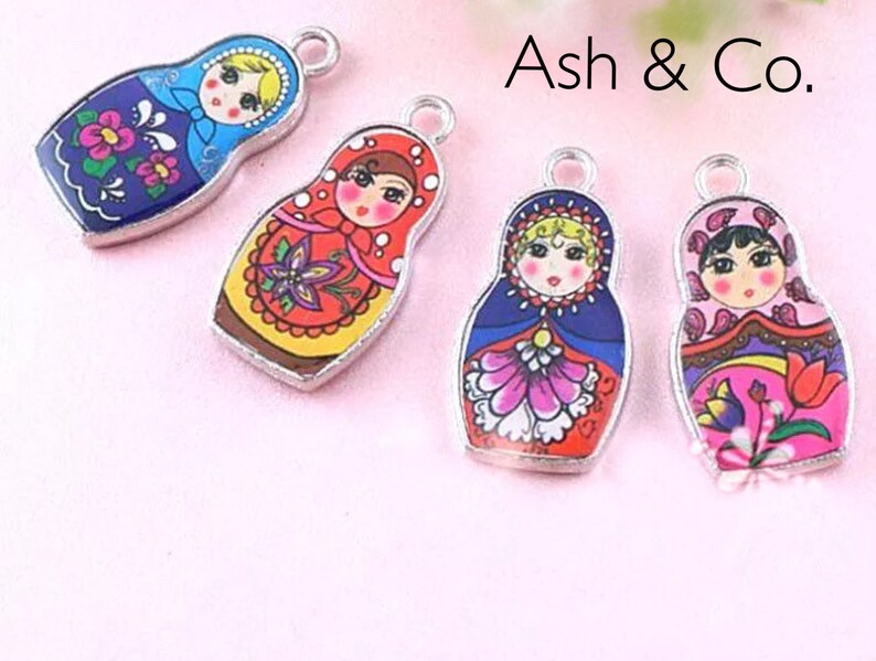 May include: Four silver charm pendants featuring Russian nesting dolls. Each doll is painted with a different colorful design and has a smiling face.
